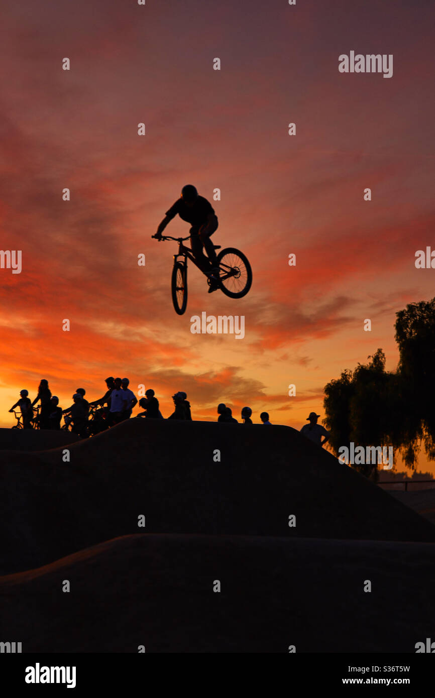 Silhouette de cycliste qui saute d'une rampe avec un ciel spectaculaire au coucher du soleil en arrière-plan. Banque D'Images