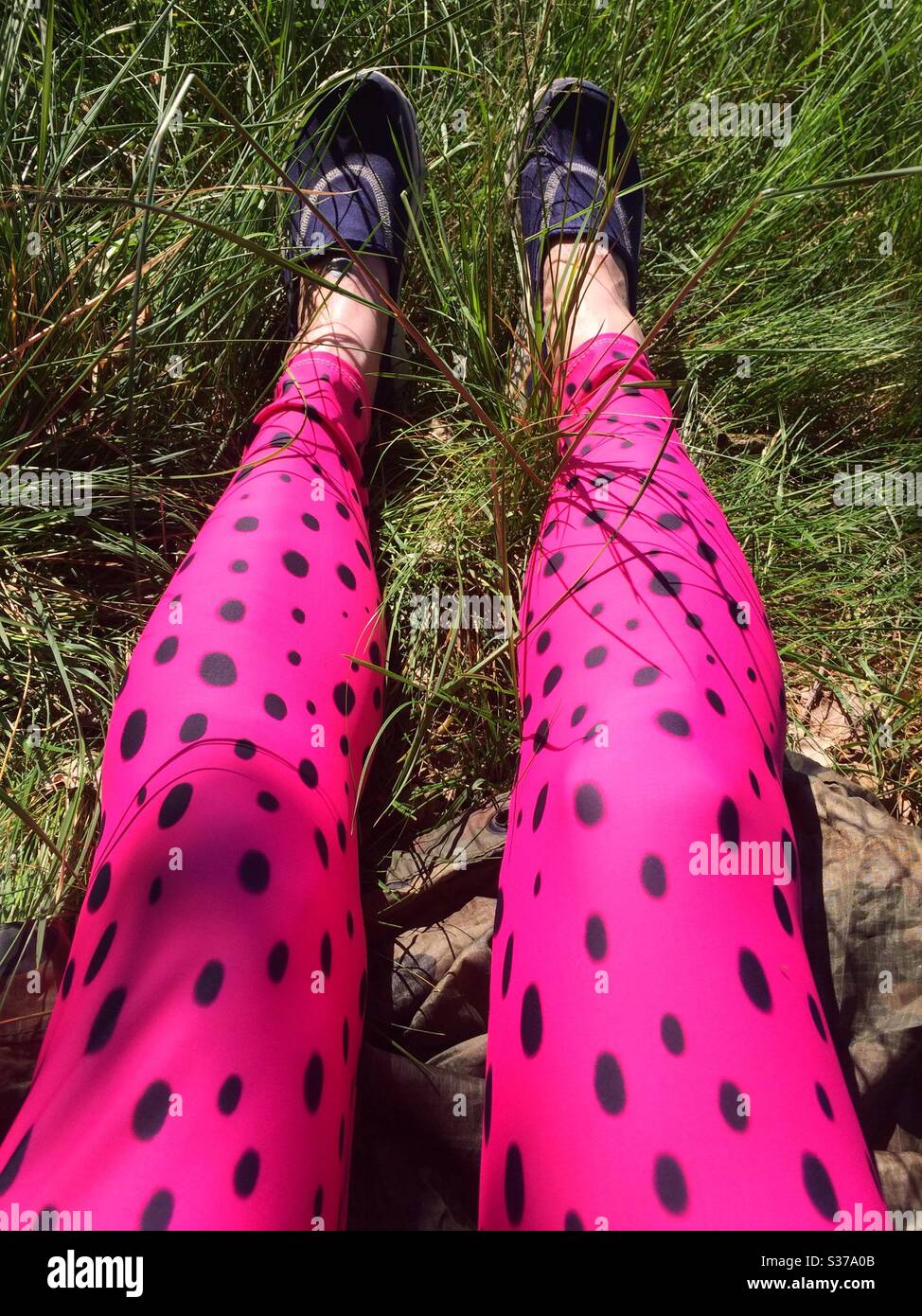 Jambes de femme assise dans une longue herbe en été, portant des leggings roses de couleur vive - Image de stock capturée avec un smartphone