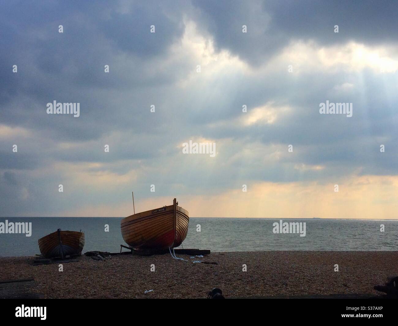 Bateau de pêche amarré sur la plage à l'aune de rayons de soleil venant à travers les nuages au-dessus de la Manche britannique Banque D'Images