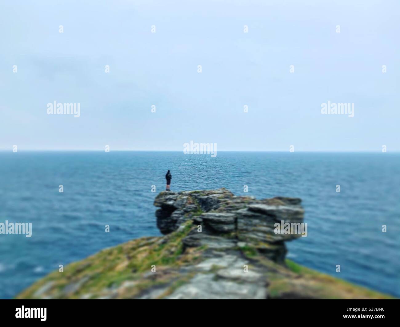 Un homme qui rassemble ses pensées sur la côte cornish à Tintagel regardant sa vue panoramique du monde. Banque D'Images