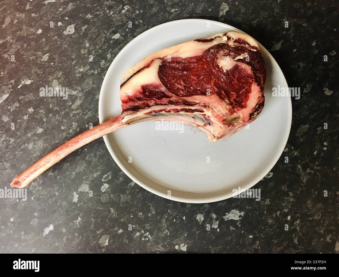 Steak Tomahawk rouge cru sur une assiette bleu d'œuf de canard avec un fond noir de plan de travail. Copier l'espace sur la plaque pour le texte Banque D'Images