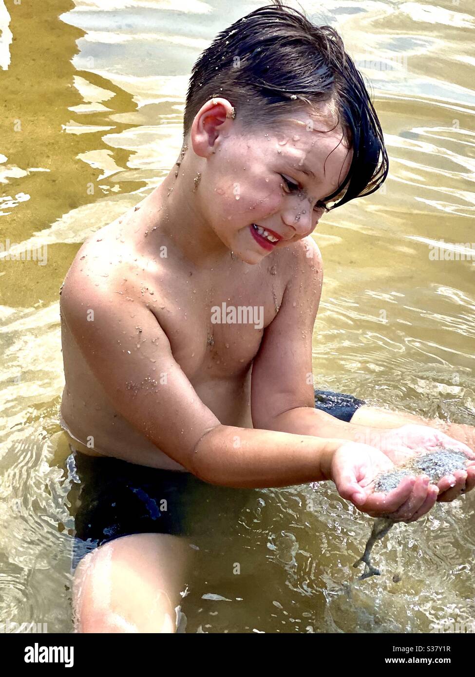 Petit garçon jouant avec du sable à la plage au lac dans l'eau Banque D'Images