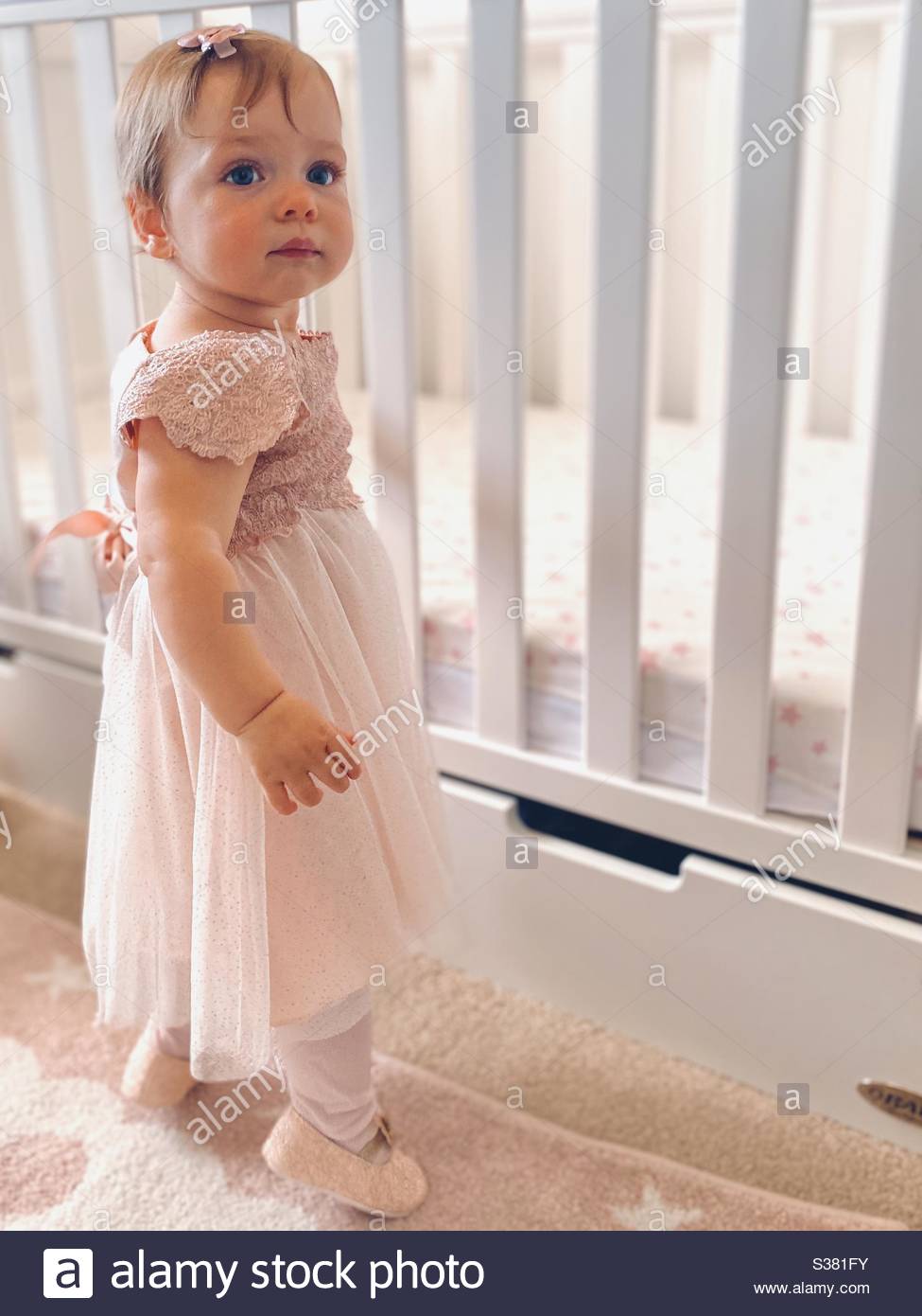 Bebe Fille Dans Une Robe Rose Jolie Debout Contre Un Lit Bebe Photo Stock Alamy