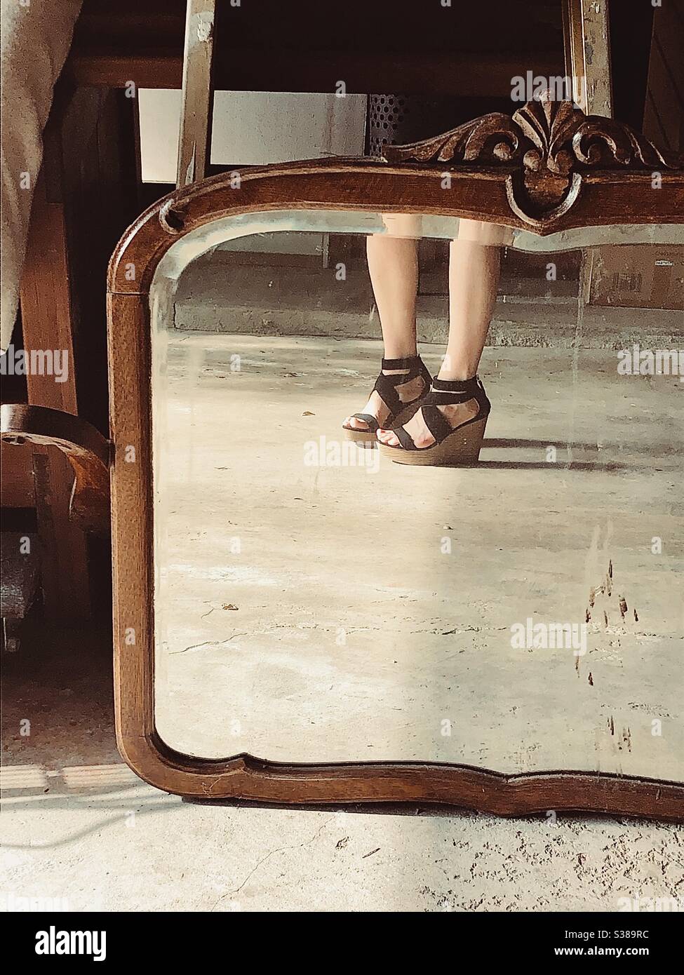 Reflet des jambes et des sandales de plate-forme d’une fille dans un miroir ancien, dans un cadre en bois. Banque D'Images