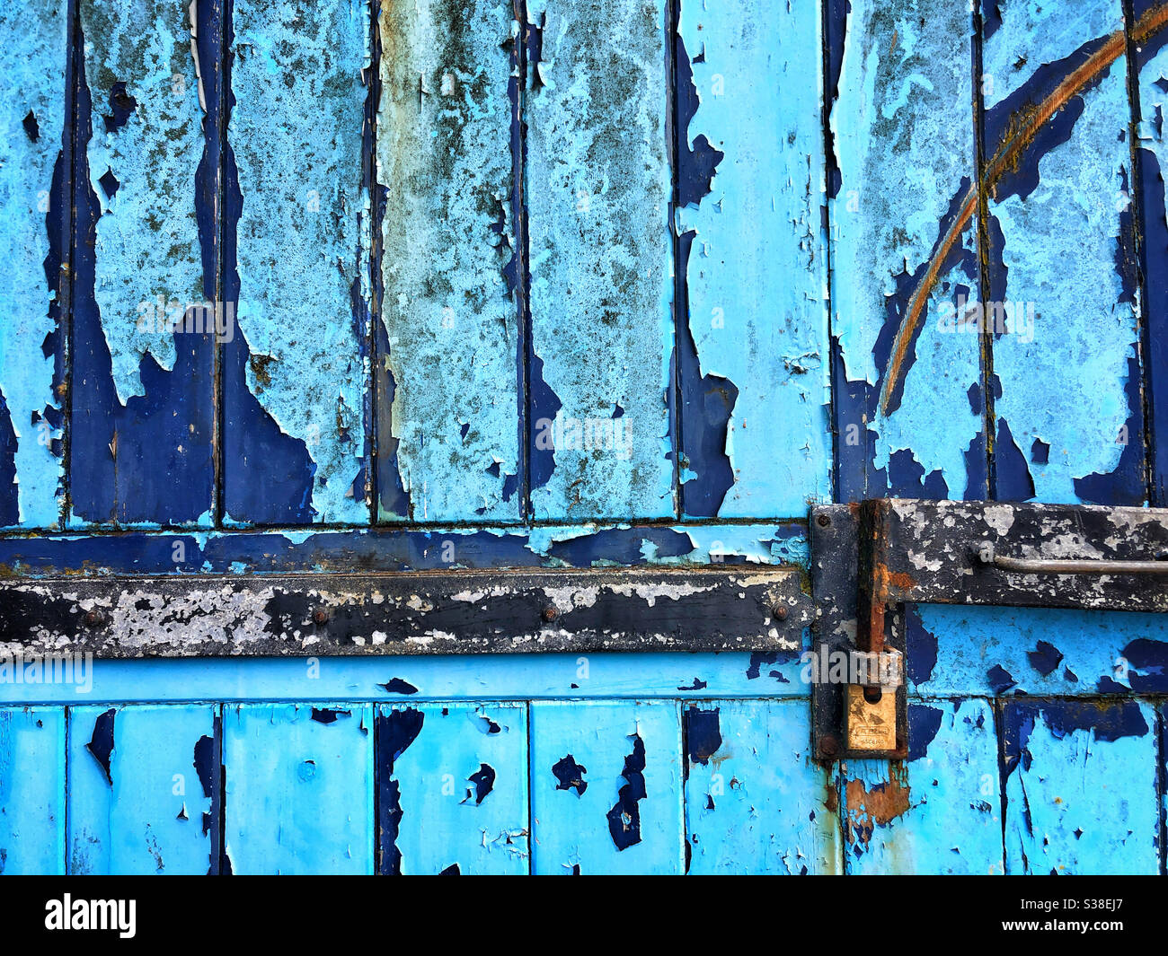 Ancienne porte de garage texturée avec peinture bleue feuilletée et cadenas Banque D'Images