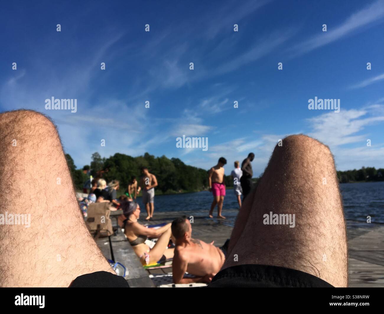 Baigneurs de soleil sur une terrasse en bois au lac de Stockholm à travers les jambes Banque D'Images