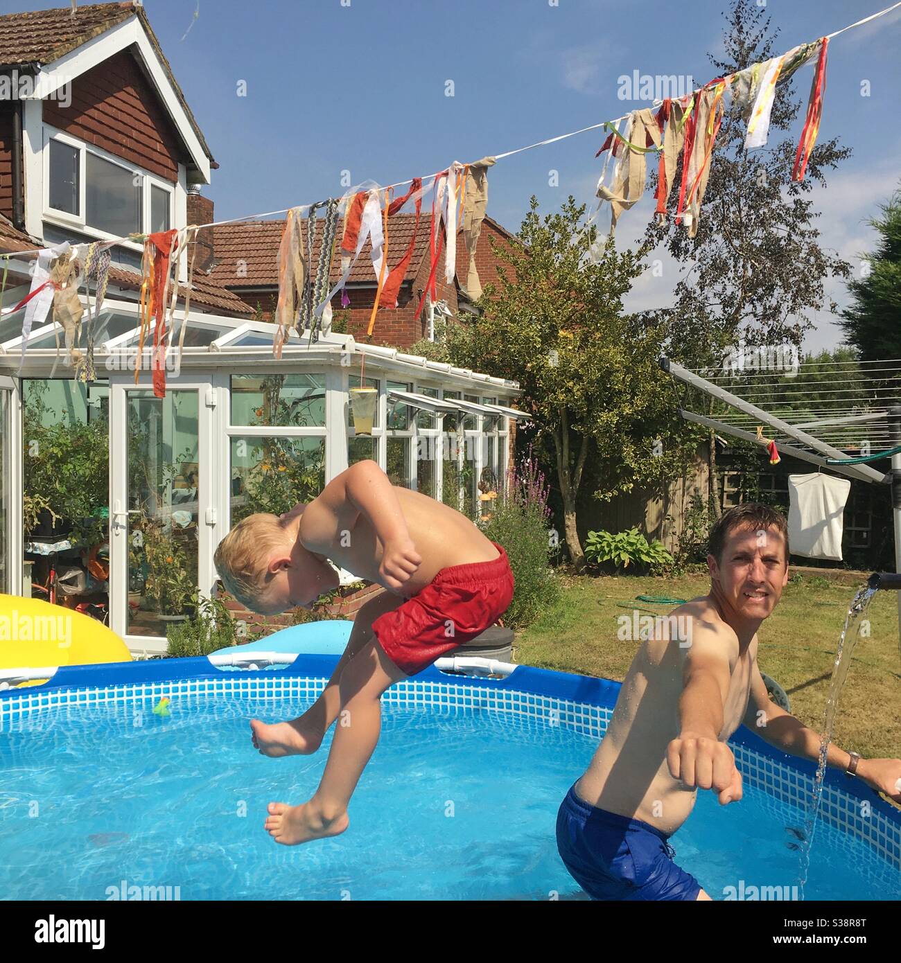 Garçon de trois ans qui saute dans une piscine de jardin. Hampshire, Angleterre, Royaume-Uni. Banque D'Images