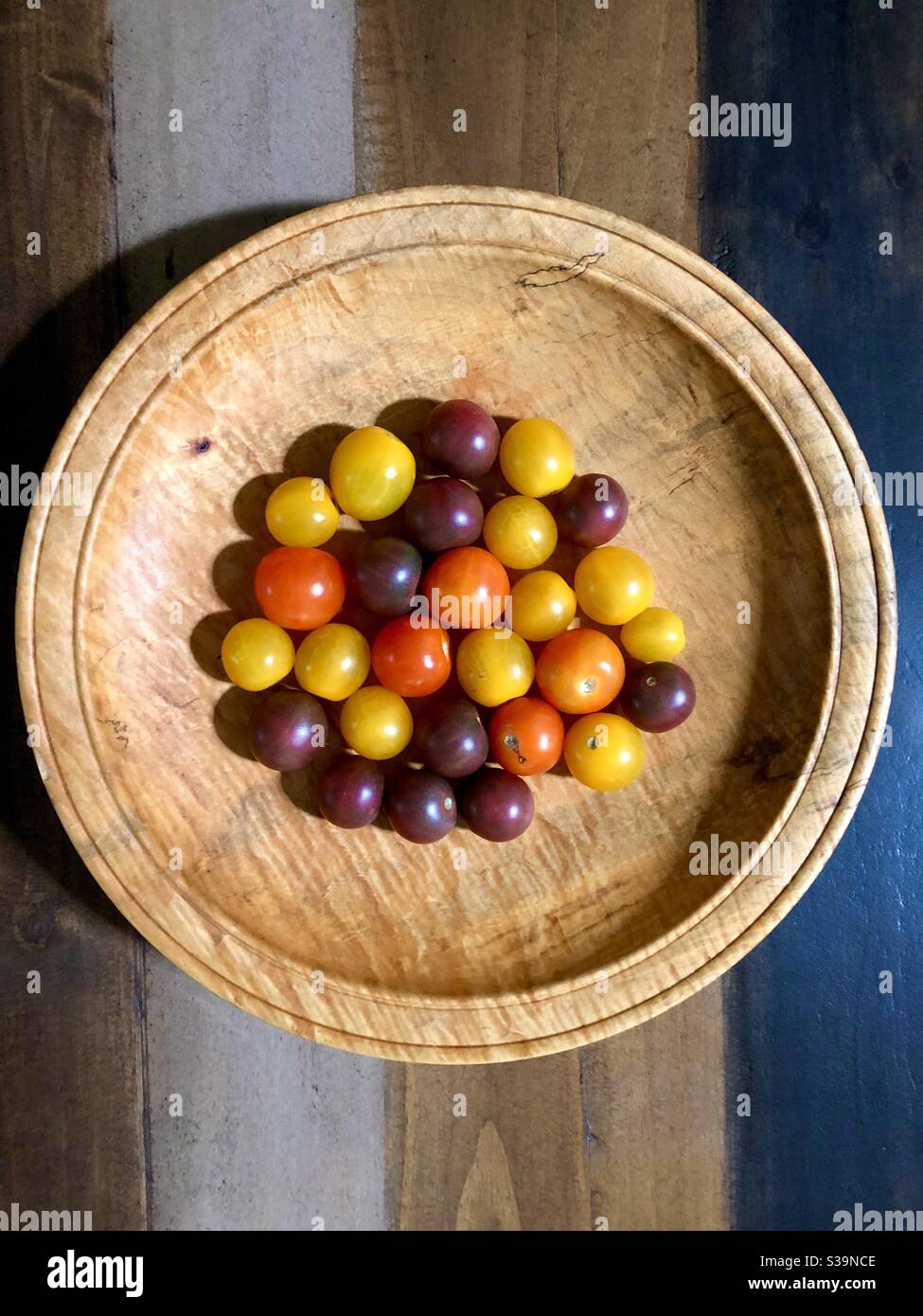 Vue d'ensemble d'une variété de tomates en fleur colorées dans un bol rond en bois. Banque D'Images