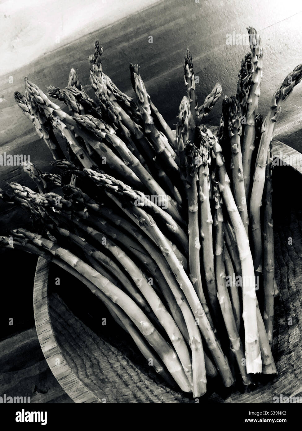Photographie monochromatique d'un bouquet d'asperges assis dans un bol en bois sur une table en bois. - Image de stock capturée avec un smartphone