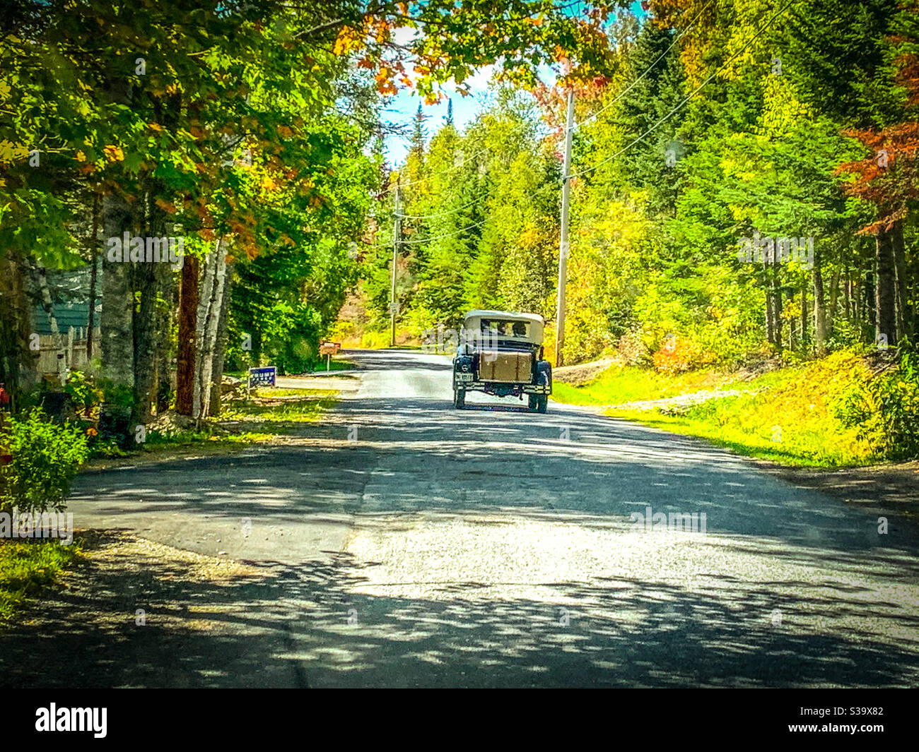 Une voiture ancienne avec un coffre sur une petite route au début de l'automne. Des signes politiques sont visibles sur le côté de la route. Banque D'Images