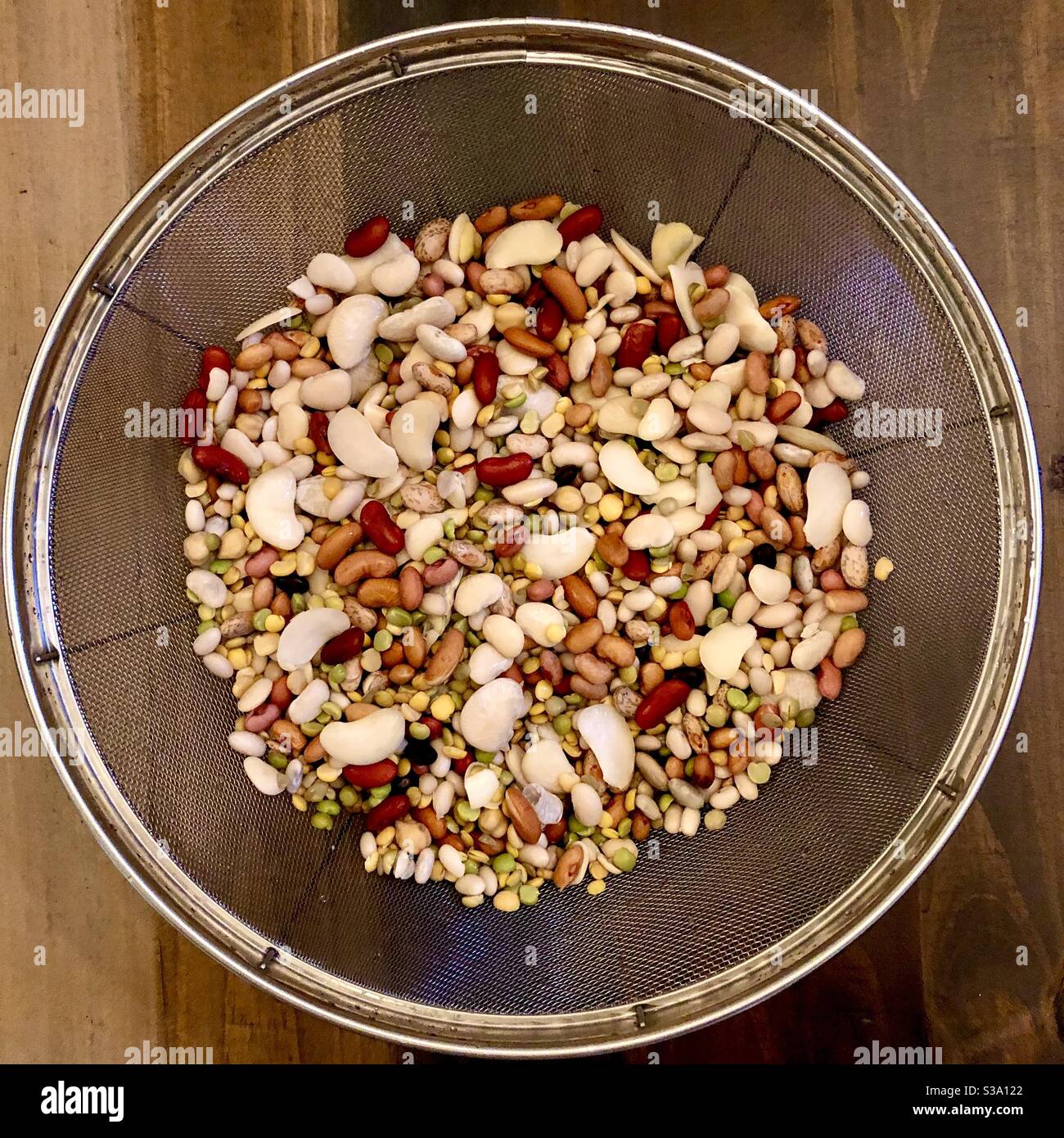 Une variété de 15 haricots secs dans une passoire circulaire sur une table en bois. Banque D'Images
