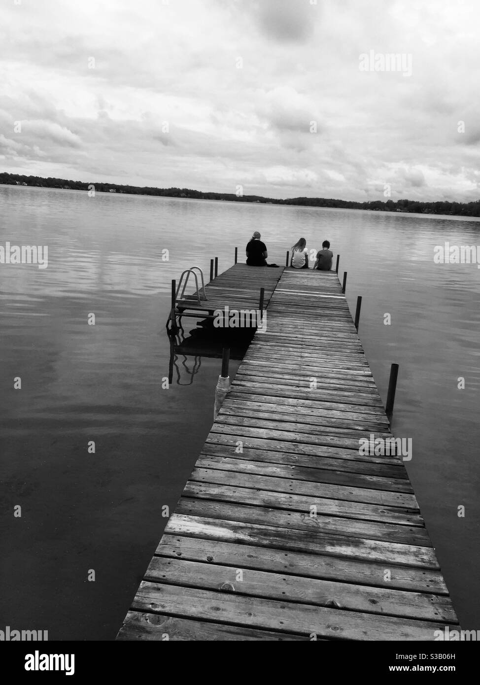 Trois enfants assis au bout d'un quai à un lac Banque D'Images
