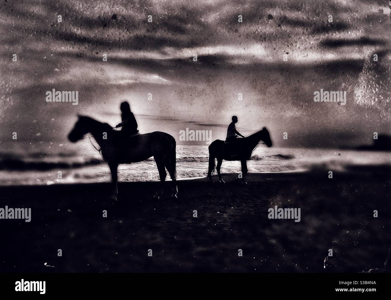 Silhouette de deux cavaliers sur leur cheval au bord de la mer. L'image est modifiée pour lui donner un aspect rétro de photographie de type tintype. Banque D'Images