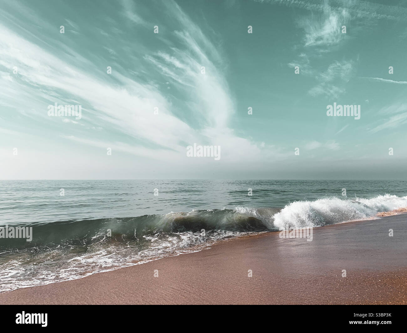 Une vague d'océan s'écrasant sur une plage de sable lors d'une journée ensoleillée. Banque D'Images