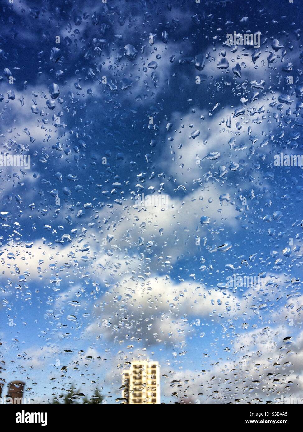 Ciel bleu et nuages blancs moelleux vus à travers une fenêtre mouiller avec des gouttes de pluie Banque D'Images