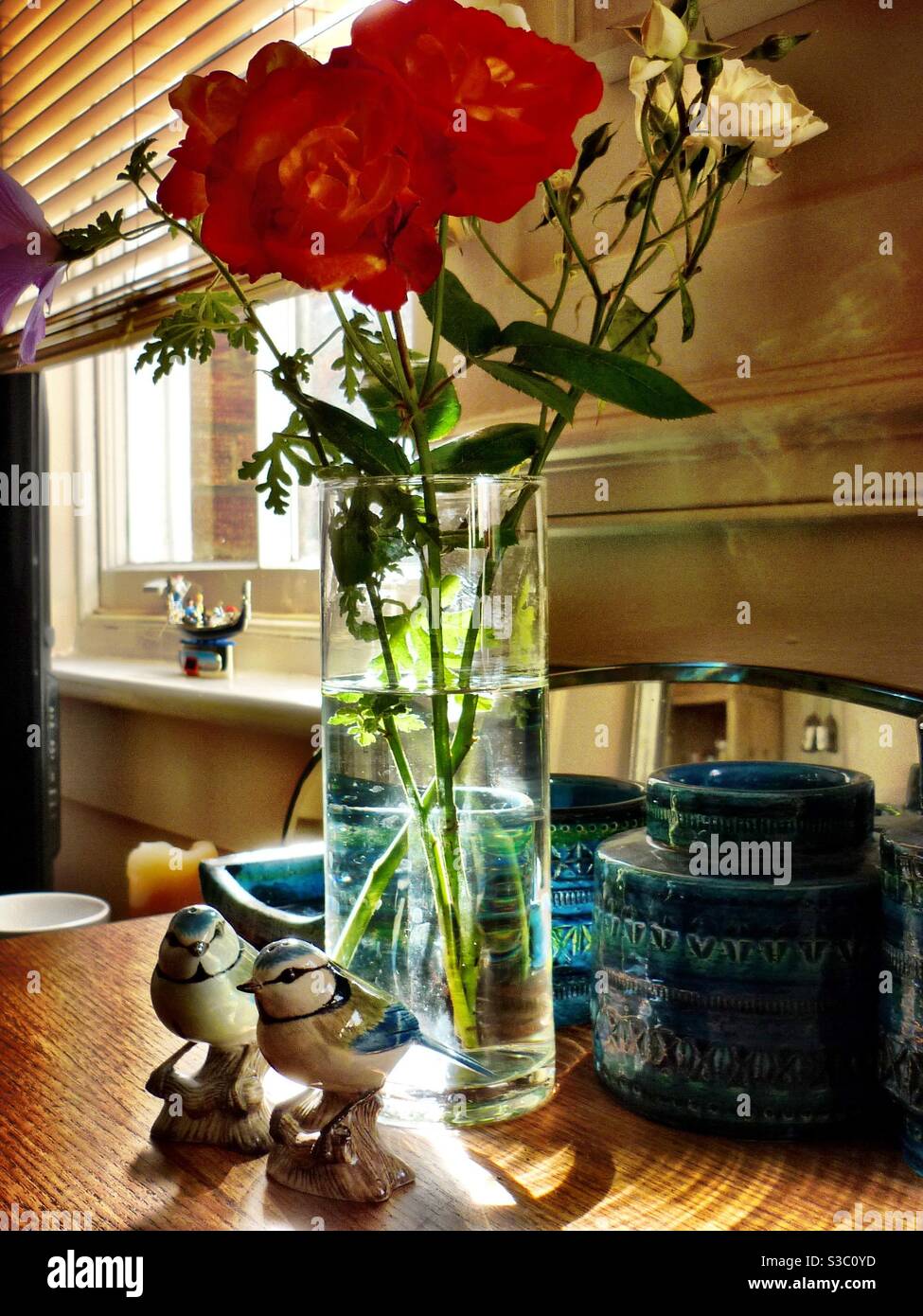 Roses rouges dans un vase avec des pots en céramique Fornasetti et sel et poivre d'oiseaux Banque D'Images