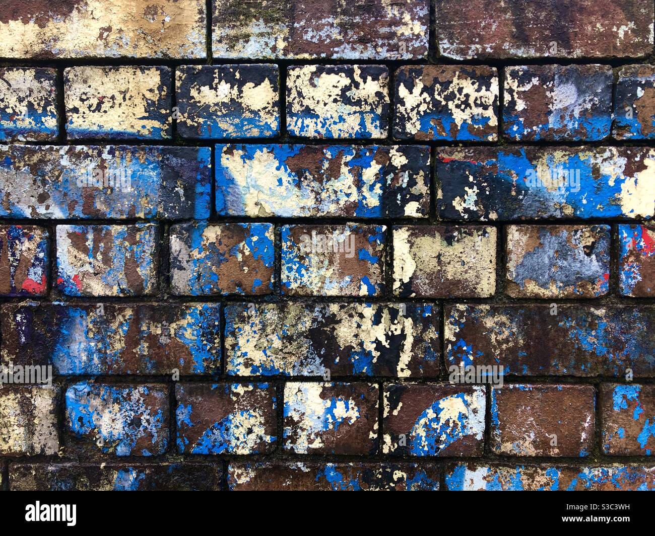 Vieux mur de briques avec des couches décolorées de graffiti peint ancien. Banque D'Images