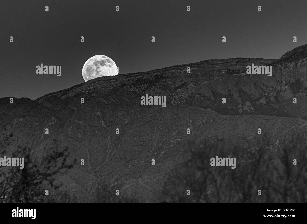 La pleine lune s'élève au-dessus des montagnes Sandia à Albuquerque, Nouveau-Mexique. Banque D'Images