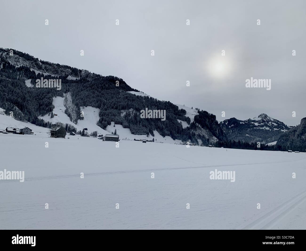 Piste de ski de fond dans le village de Studen en Suisse entourée de montagnes. Un paysage en hiver sous la neige. Le ciel est couvert et le soleil est flou. Banque D'Images