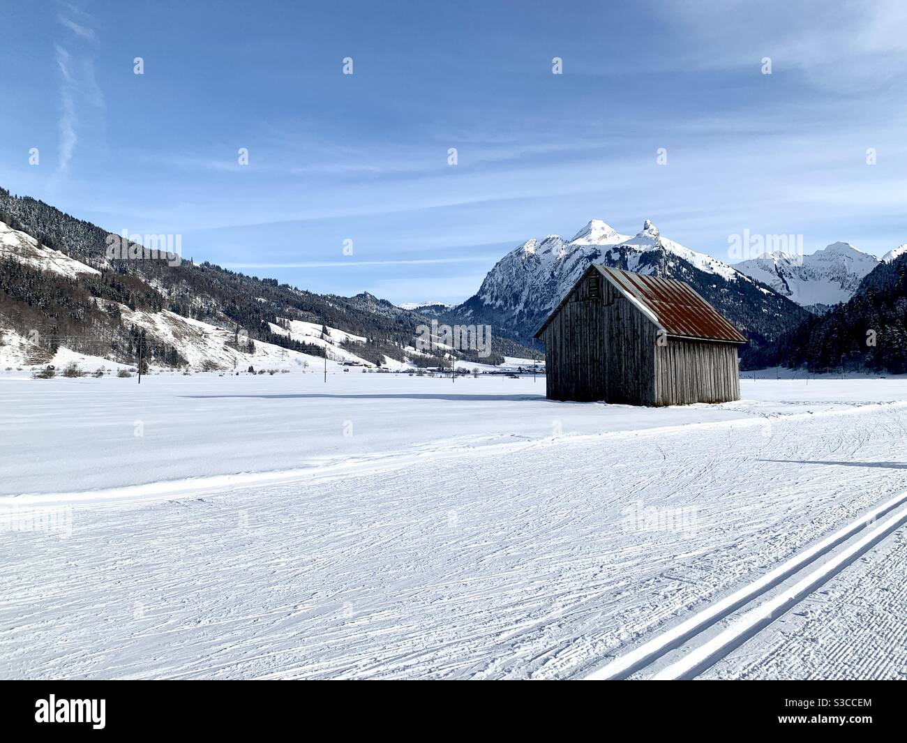 Grange abandonnée sur la plaine dans le village de Studen, Suisse en hiver. Le sol et les montagnes qui l'entourent sont couverts de neige. Le ciel a quelques nuages de cirrus. Banque D'Images