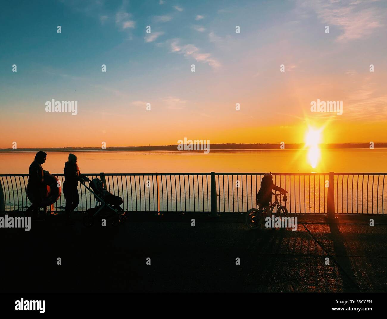Une famille marchant le long de la rivière Mersey silhouetted par le coucher du soleil. Exercice quotidien de verrouillage - Image de stock capturée avec un smartphone
