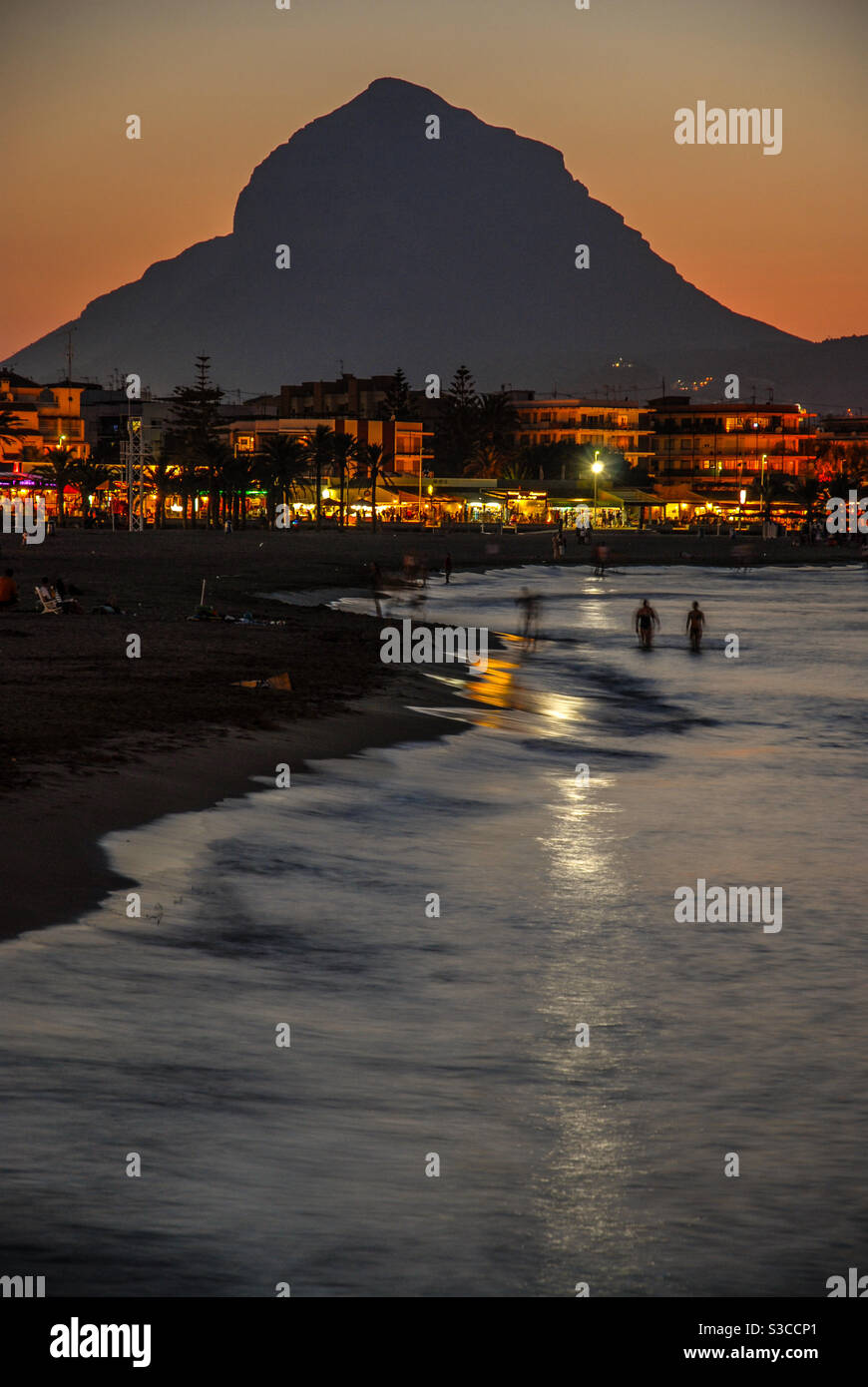 Arenal scène de plage avec des gens dans la mer et coucher de soleil derrière la montagne Montgo, Javea, province d'Alicante, Espagne Banque D'Images