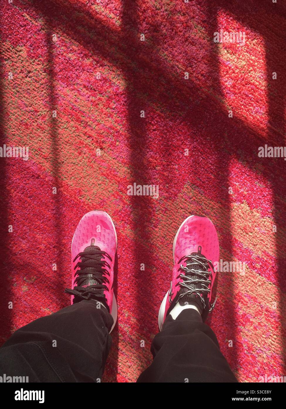 Femme portant des chaussures de sport rose chaud sur un tapis rouge vif à motifs, États-Unis - Image de stock capturée avec un smartphone