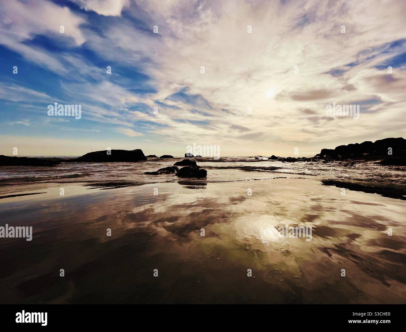 Paysage marin spectaculaire avec des nuages et le ciel se reflétant dans les eaux peu profondes tandis que de douces vagues se roulent. Banque D'Images