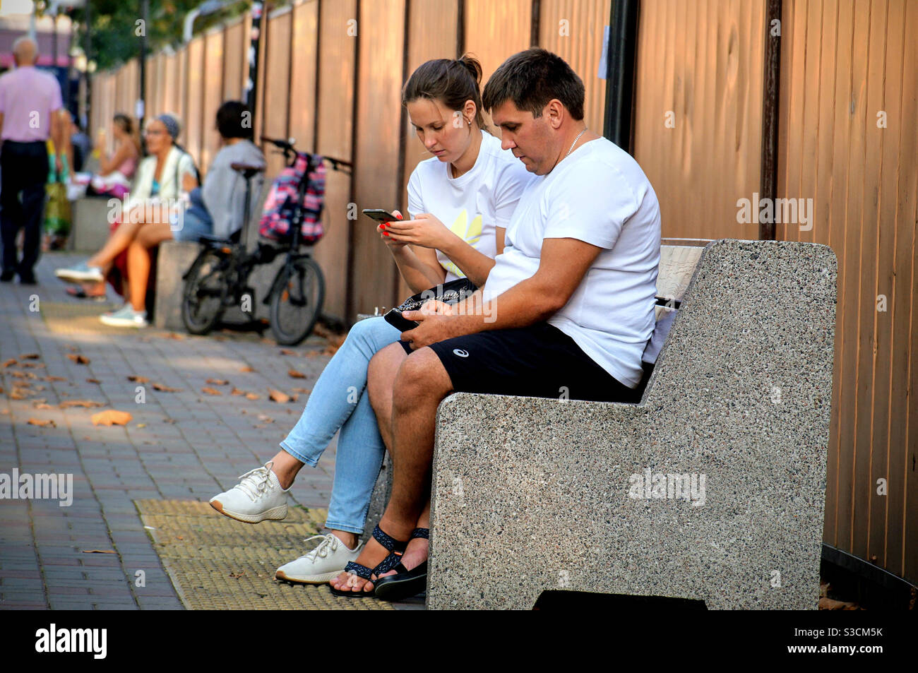 Un jeune homme avec une fille en T-shirts légers sont assis sur un banc avec téléphones Banque D'Images