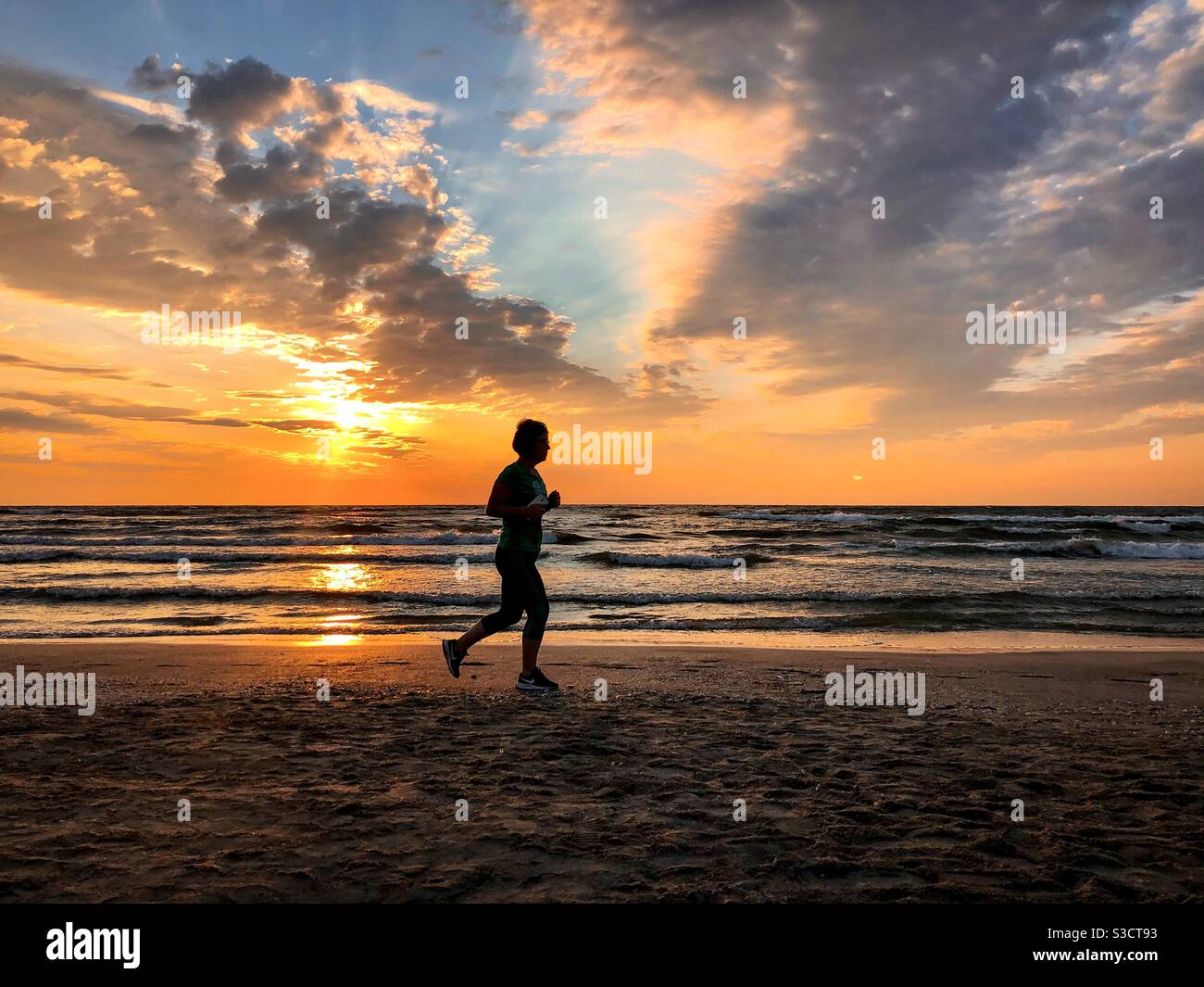 Silhouette de femme qui fait du jogging sur la plage au lever du soleil Banque D'Images