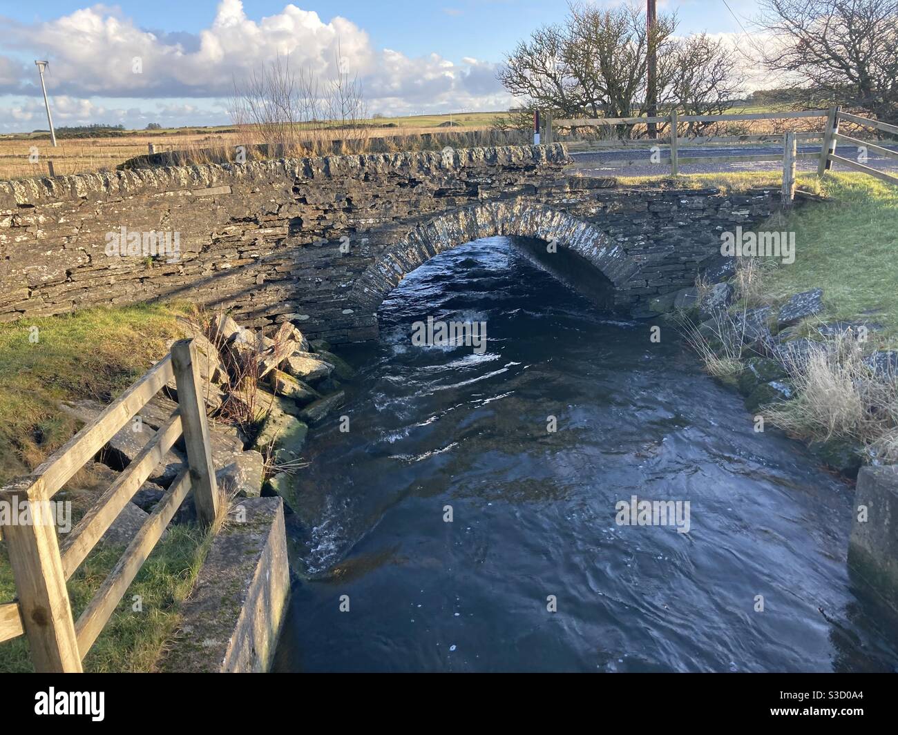 Un ruisseau de babouille qui passe sous un pont de pierre par une journée d'hiver claire. Banque D'Images