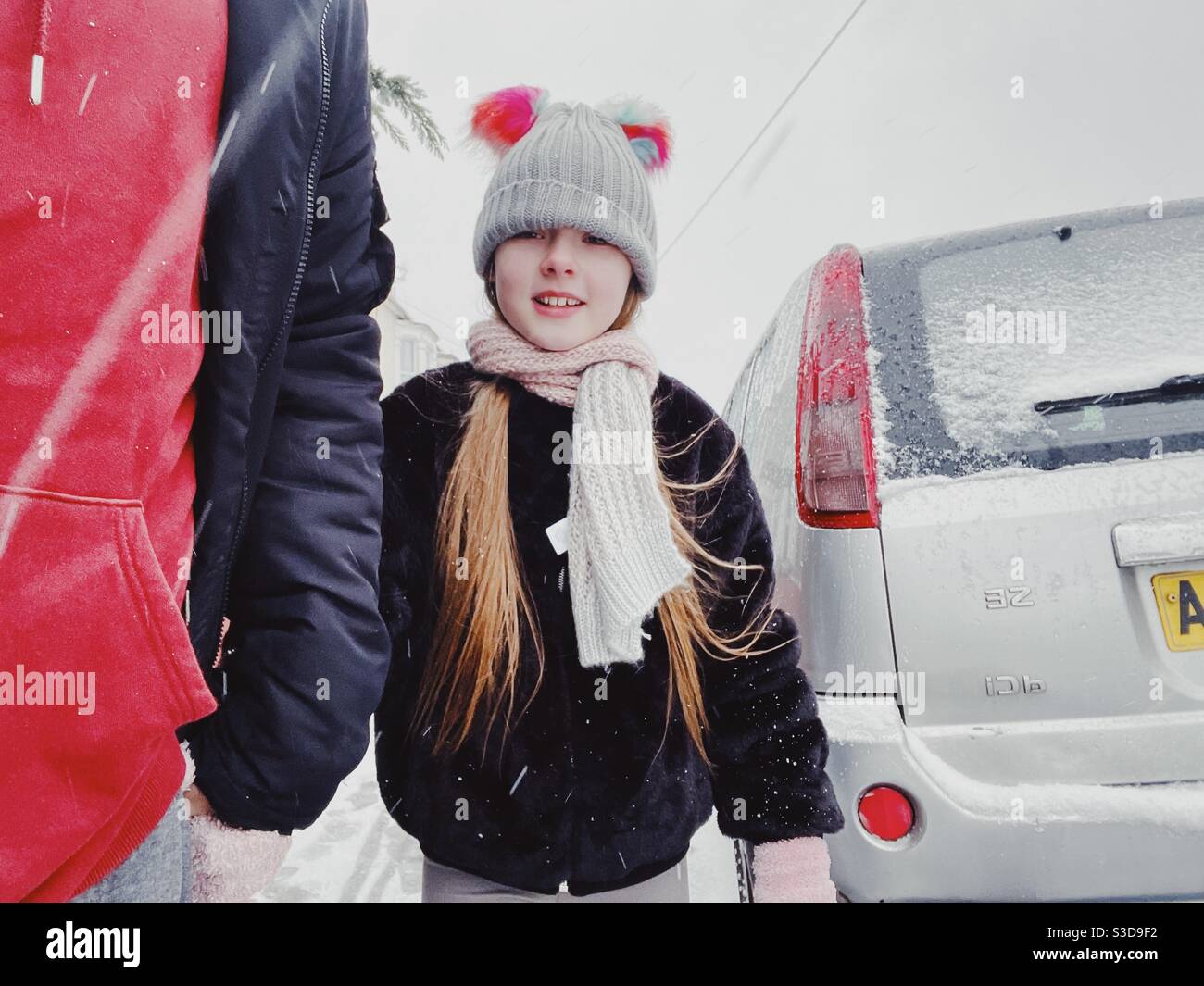 Fille regarde la caméra tout en tenant la main du père dans la neige Banque D'Images