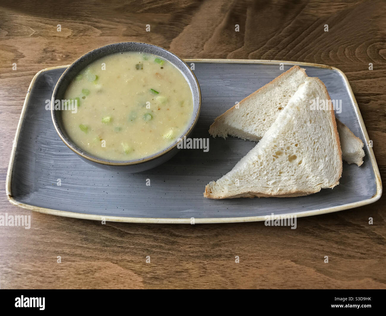 Une soupe artisanale de légumes, avec de la patate douce, du poireau, de la pomme et du céleri, est présentée à côté de deux tranches de pain blanc, plaquées sur une table dans un café. Banque D'Images