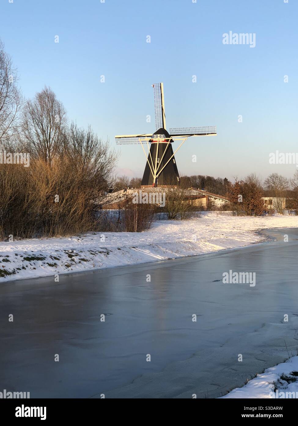 Moulin à vent hollandais traditionnel assis à côté d'un canal gelé sous un ciel bleu d'hiver Banque D'Images