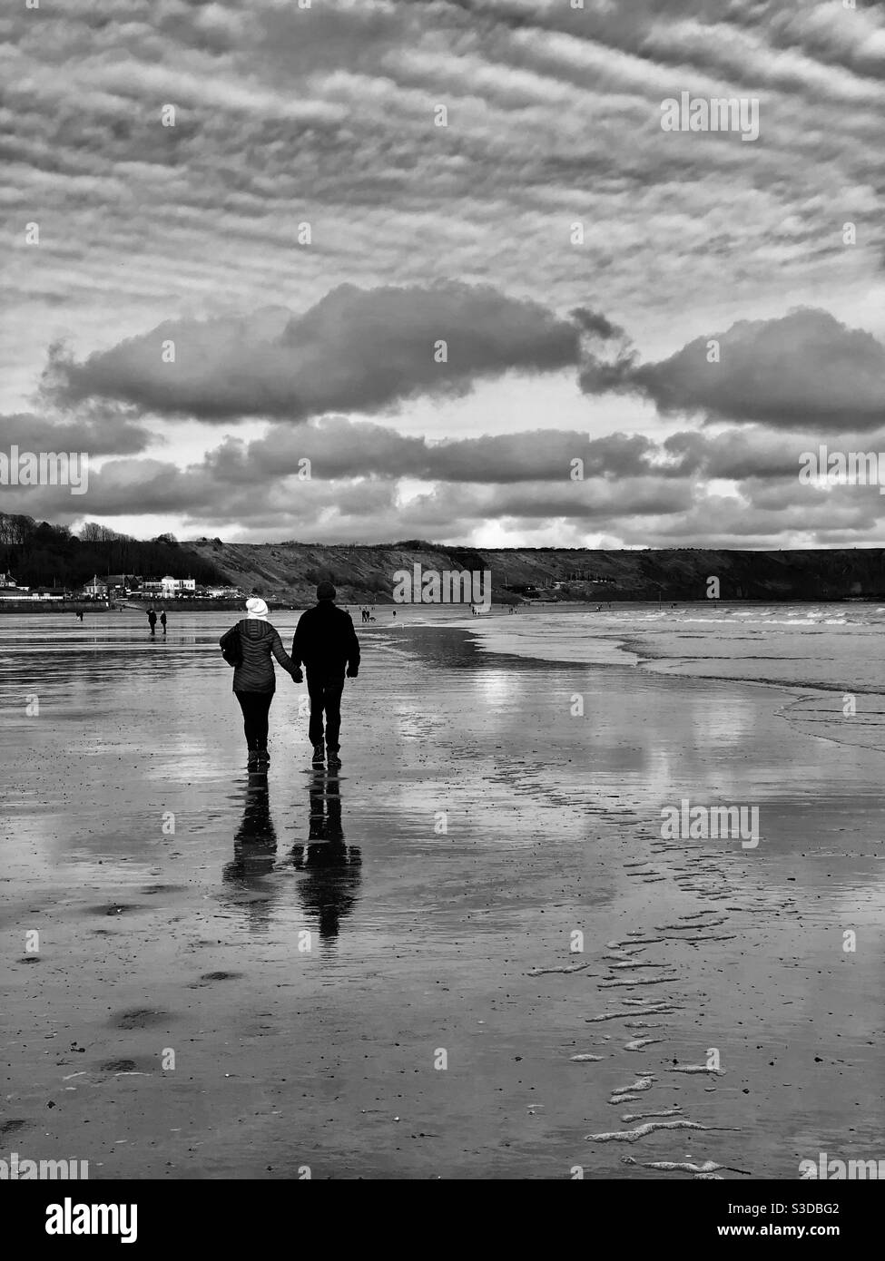 Photo noir et blanc d'un couple tenant les mains pendant marche le long d'une plage en hiver Banque D'Images