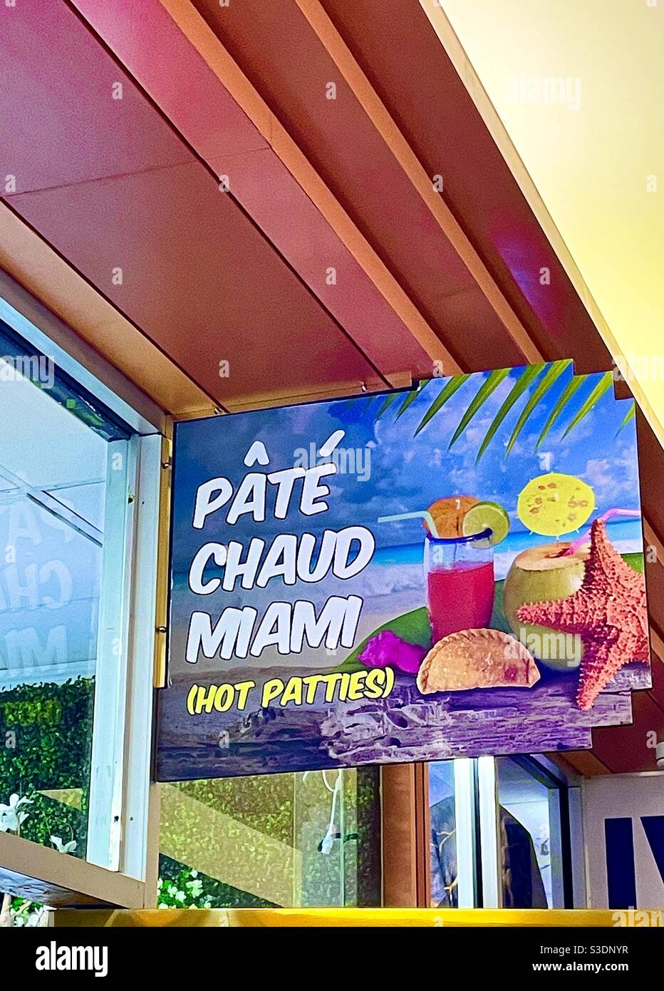 Il s'agit d'un panneau captivant et coloré annonçant le Pate Chaud Miami (hot patties) avec une photo d'une boisson tropicale, d'une empanada et d'une étoile de mer au-dessus d'un magasin dans le centre commercial de l'hôtel Doubletree - Image de stock capturée avec un smartphone