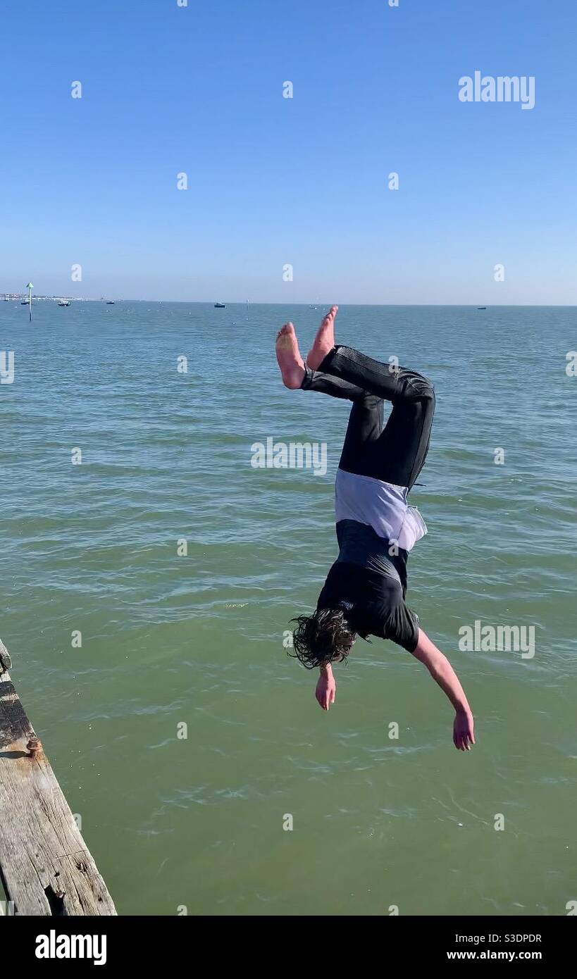 Un adolescent sautant de la jetée vers la mer à l'envers en plongée Banque D'Images