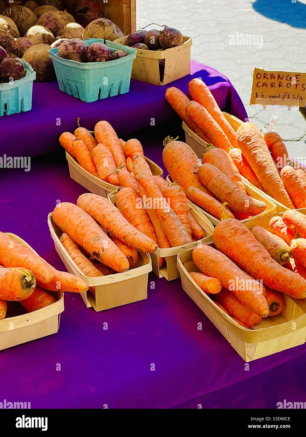 Énormes carottes et betteraves orange locales dans de petits paniers sur une table mauve, avec un panneau imprimé à la main sur un stand de légumes du marché agricole Union Square, Manhattan, NewYork, États-Unis. - Image de stock capturée avec un smartphone