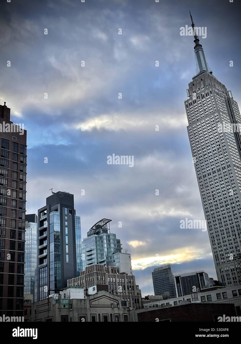 Un éclat de lumière du soleil à travers les nuages gris doux derrière l'Empire State Building dans Midtown Manhattan lors d'une journée froide en mars. Banque D'Images