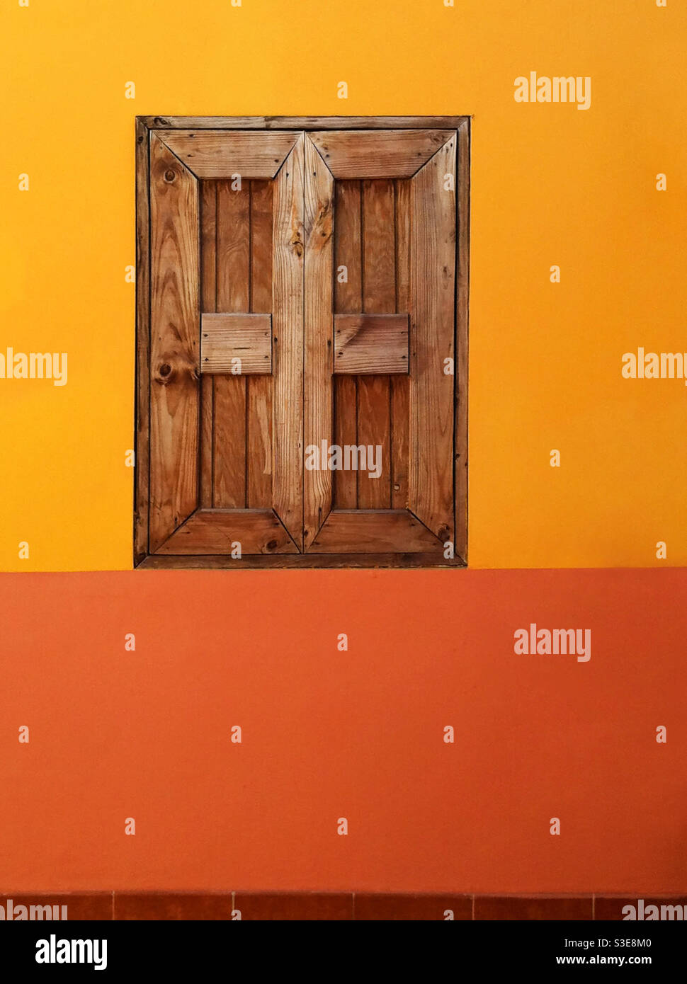 Des volets en bois massif couvrent une fenêtre dans un mur aux couleurs chaudes. Jamaïque. Banque D'Images