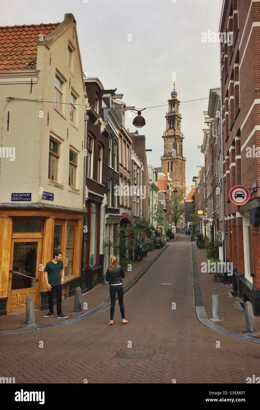 Un jeune couple se tient dans la rue du quartier Jordaan d'Amsterdam, avec le Westerkerk en arrière-plan Banque D'Images