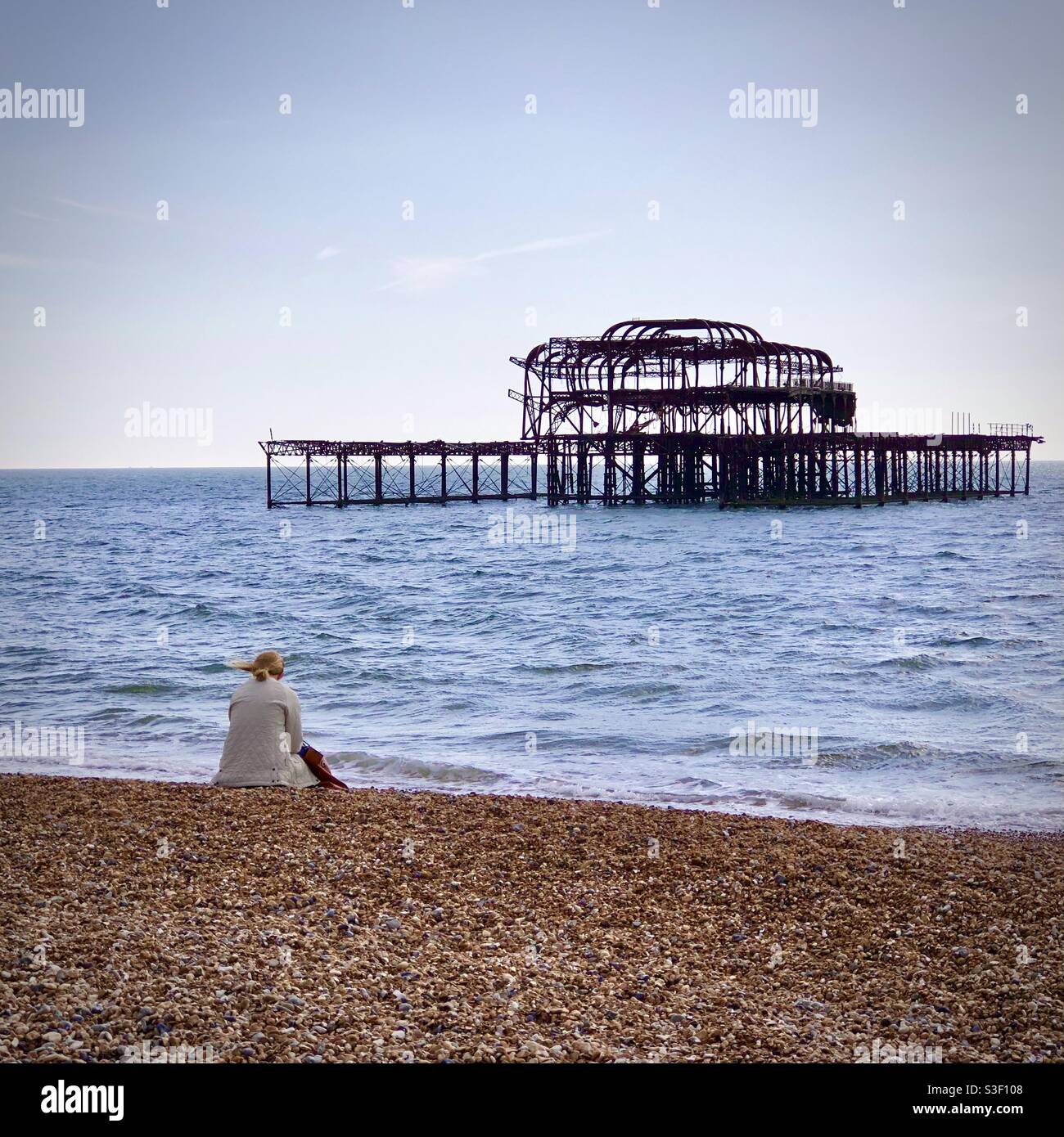 Femme assise sur la plage de Brighton sur les ruines de l'ancien West Pier Sussex, Royaume-Uni Banque D'Images