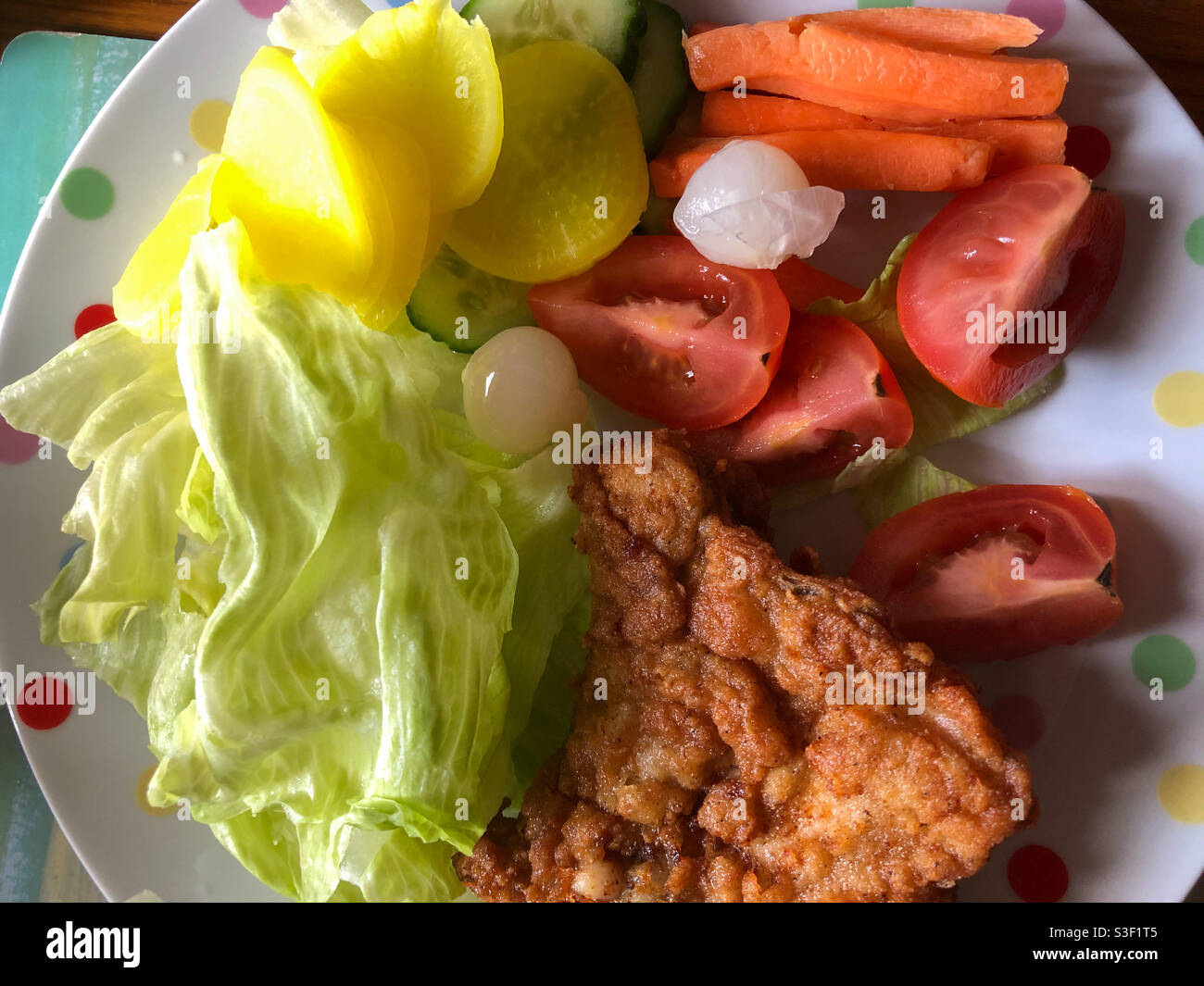 Un morceau de poulet frit avec une salade comprenant de la laitue, des tranches de tomate, des carottes crues, du radis mariné sur une assiette. Banque D'Images