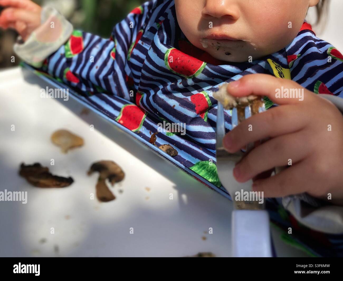 Bébé/tout-petit mangeant des champignons dans une chaise haute tenant un fourche Banque D'Images