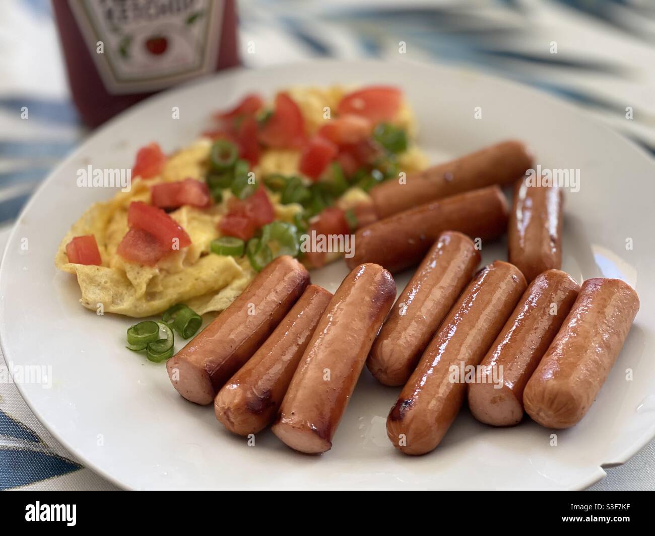 Hot dogs Wieners avec un côté d'omelette recouvert de tomates et d'oignons verts sur une assiette blanche. Ketchup sur le côté. - Image de stock capturée avec un smartphone