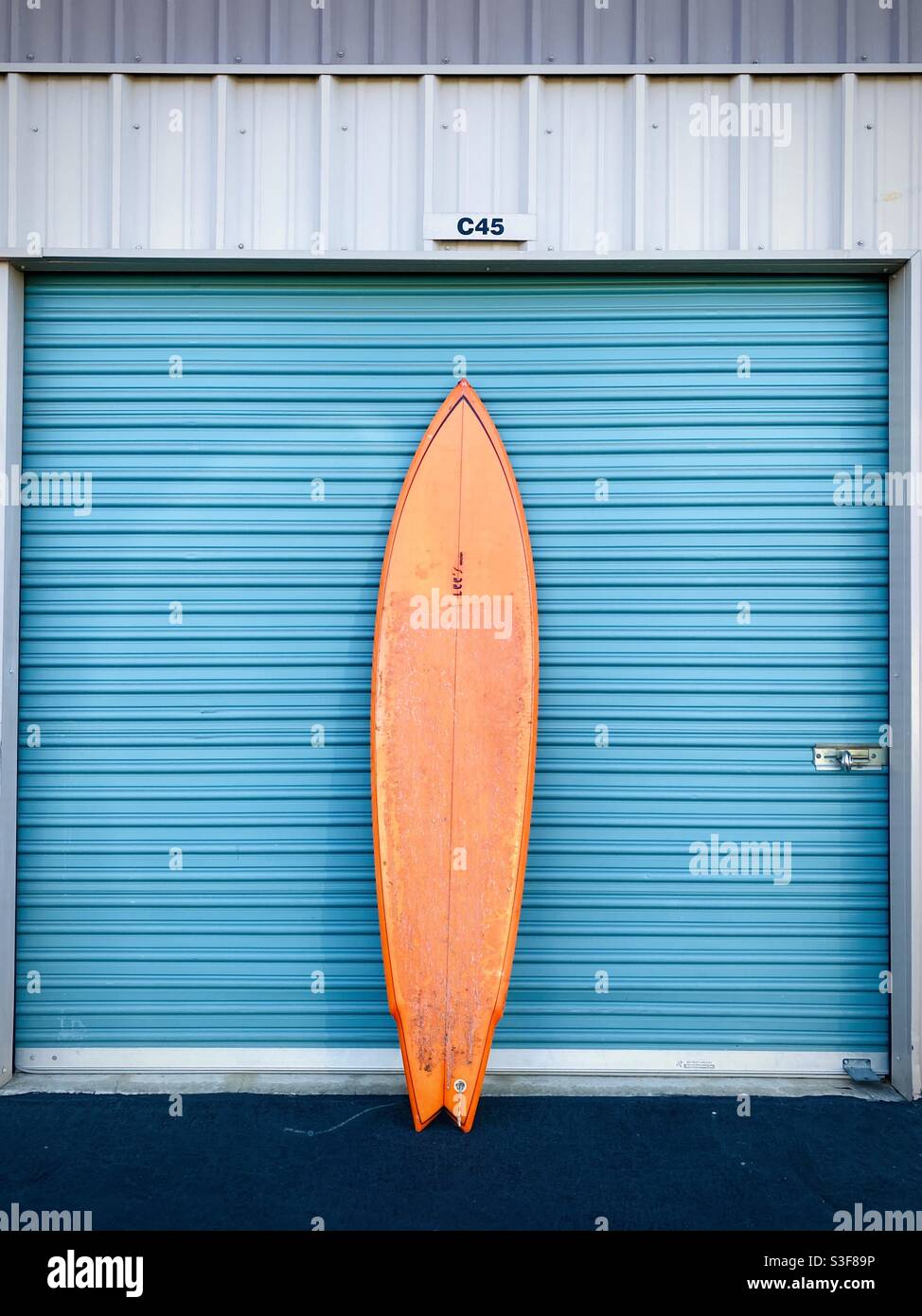 Une planche de surf orange contre un garage. Banque D'Images