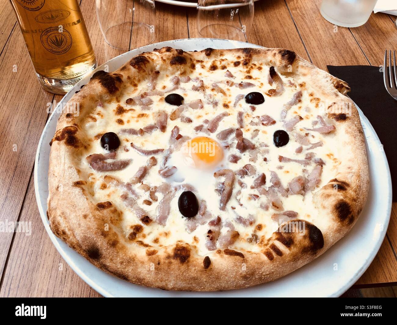 Pizza à base d'oignon et de bacon à base de crème recouverte d'olives  noires un œuf craqué, avec un verre de bière dans un restaurant français à  Palavas les Flots près de