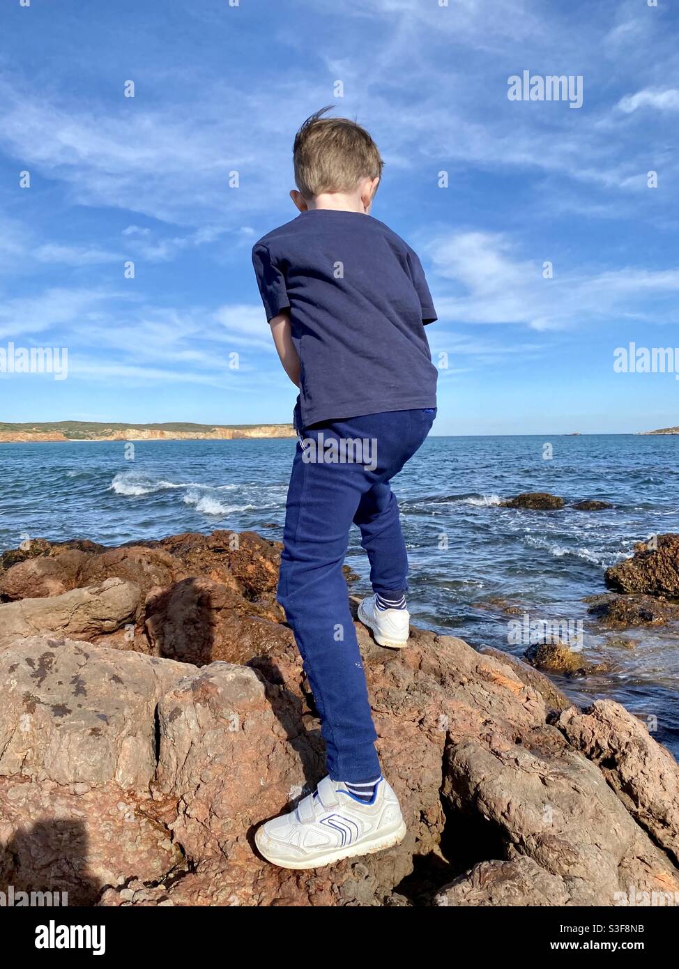 Petit garçon debout sur des rochers au bord de la mer et regardant pour la vie en mer Banque D'Images