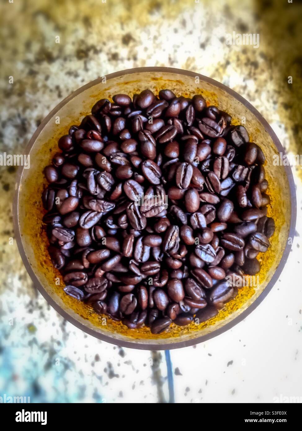 Grains de café Arabica fraîchement torréfiés dans un bol rond sur un comptoir en granit. Cultivé et exporté principalement par les pays en développement, il est consommé principalement dans les pays développés. - Image de stock capturée avec un smartphone