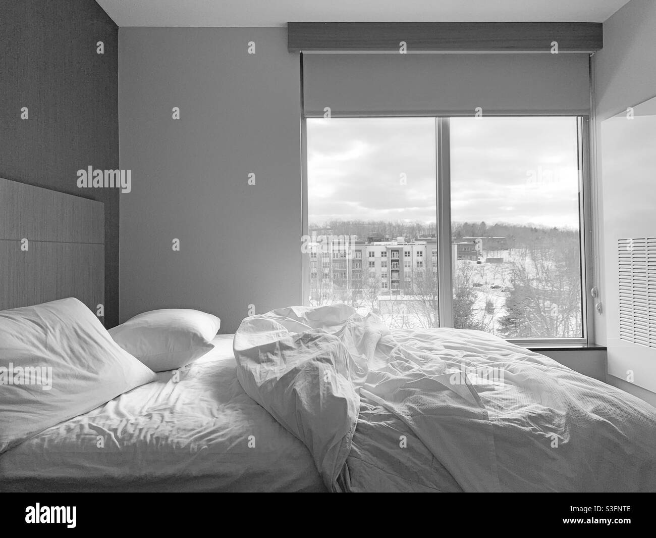 Image en noir et blanc d'un lit avec des draps rumbolés dans une chambre au design minimaliste - Image de stock capturée avec un smartphone